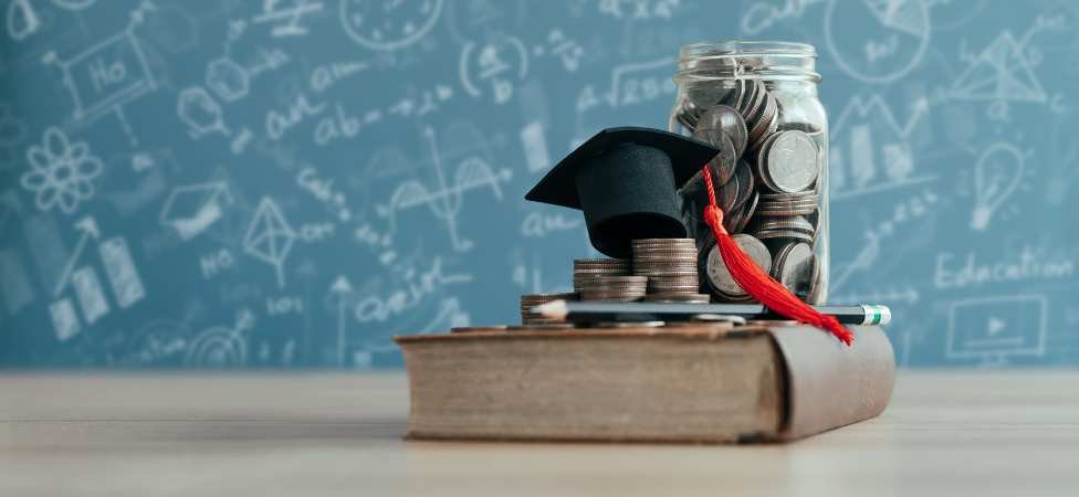 libro, dinero y sombrero y birrete sobre una mesa